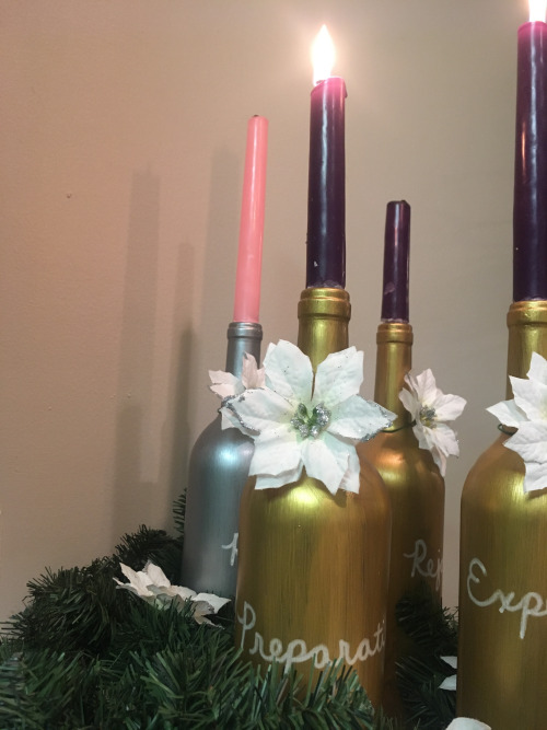 4 gold painted wine bottles and a silver one holding purple and pink candles